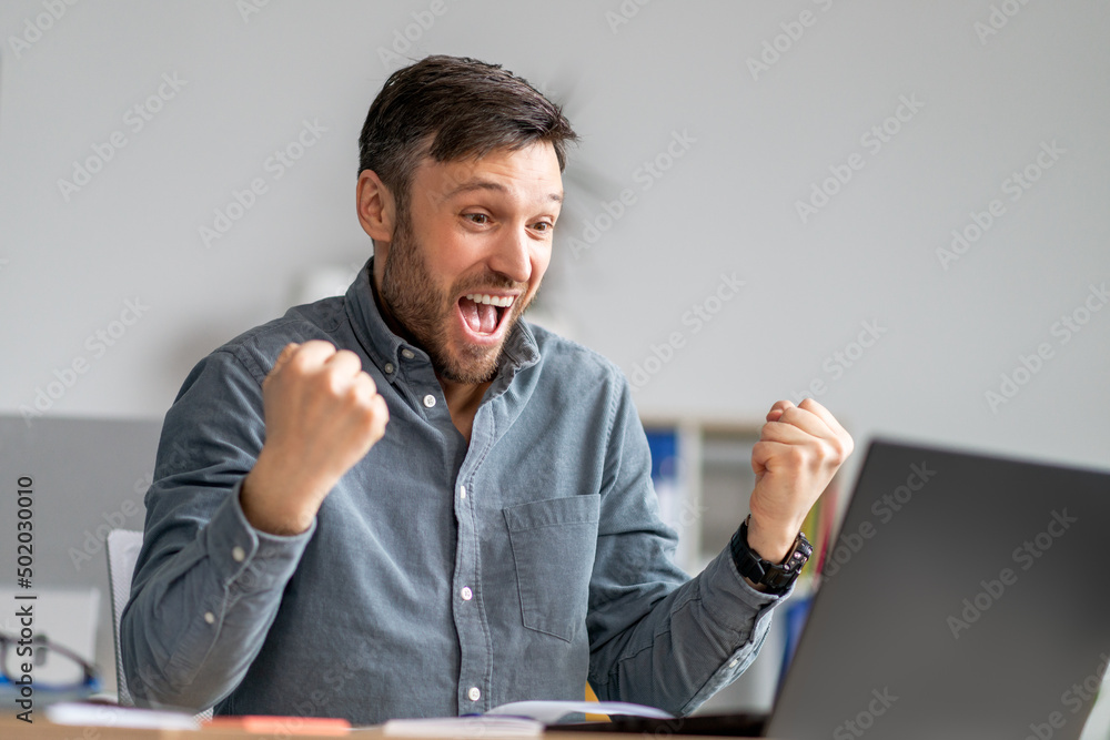 Business luck. Overjoyed mature businessman using laptop and shaking fists, celebrating great news, sitting in office Business luck. Overjoyed mature businessman using laptop and shaking fists, celebrating great news, sitting in office