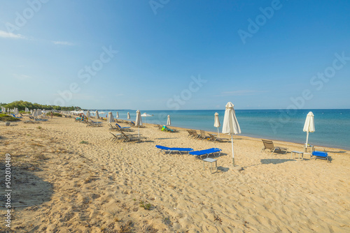 Beautiful view of empty sandy beach with sun loungers and parasols on Mediterranean coast. Greece.