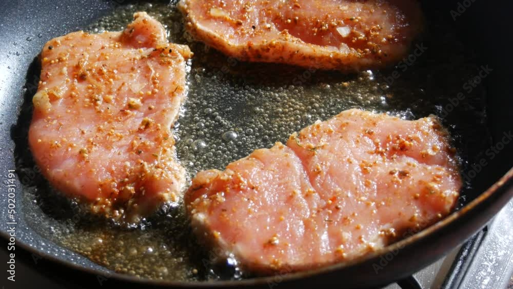 A large piece of pork schnitzel meat with seasonings is fried in a pan in a home kitchen. Close up view A large piece of pork schnitzel meat with seasonings is fried in a pan in a home kitchen. Close up view