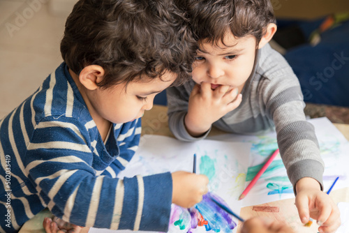 twin children painting with colored pencils and paints