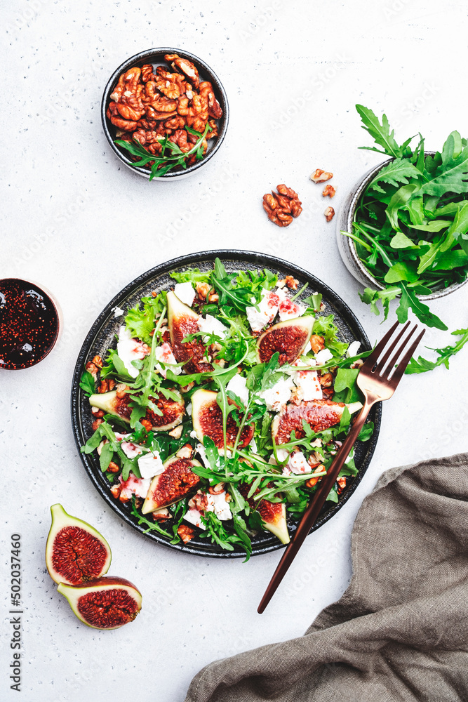 Delicious summer salad with sweet  figs, white feta cheese, walnuts, arugula and jam vinegar dressing on white table background, top view, negative space