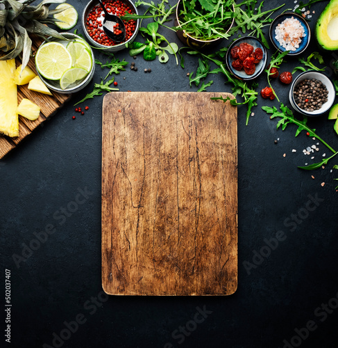 Fototapeta Naklejka Na Ścianę i Meble -  Healthy eating food layout and diet nutrition concept. Pineapple, vegetables, dried fruits, greens and other ingredients for salad preparation on black table background with wooden board