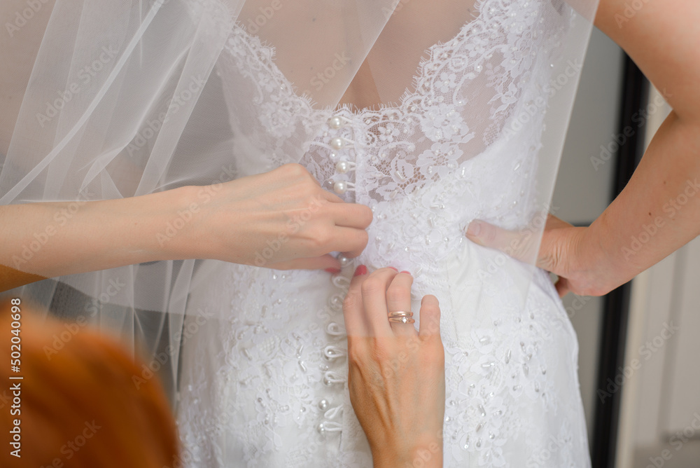 The bridesmaids help the bride put on her wedding dress. Close-up of hands The bridesmaids help the bride put on her wedding dress. Close-up of hands