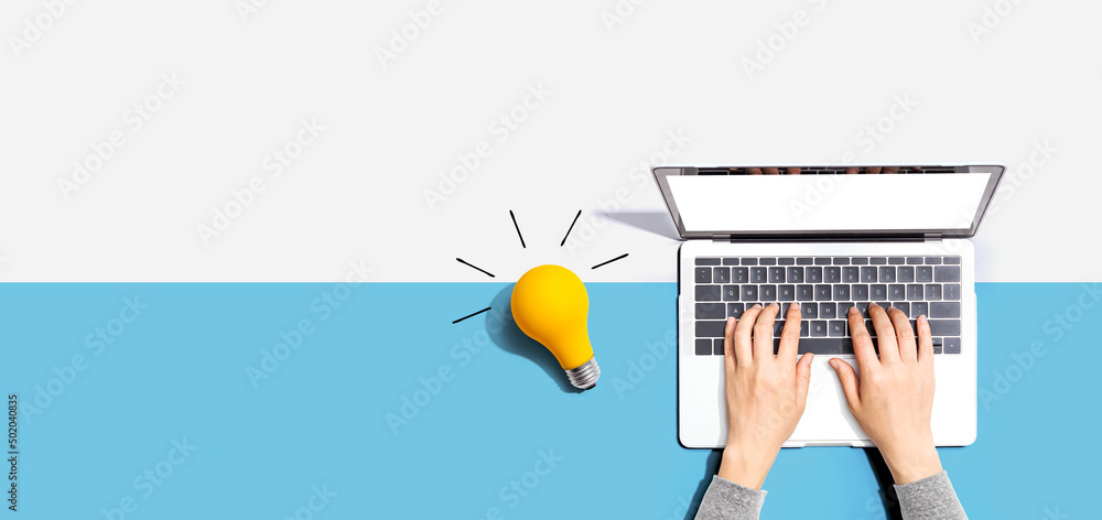 Person using a laptop computer and a light bulb - Flat lay - obrazy, fototapety, plakaty 