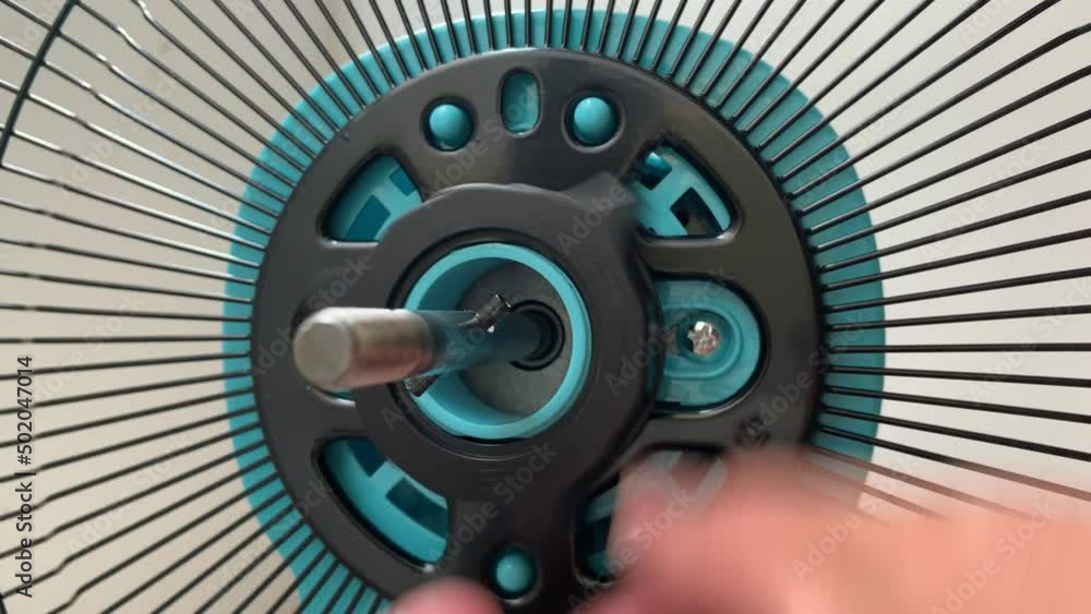 Tighten black plastic nut at rear grille bar on blue desk electric fan