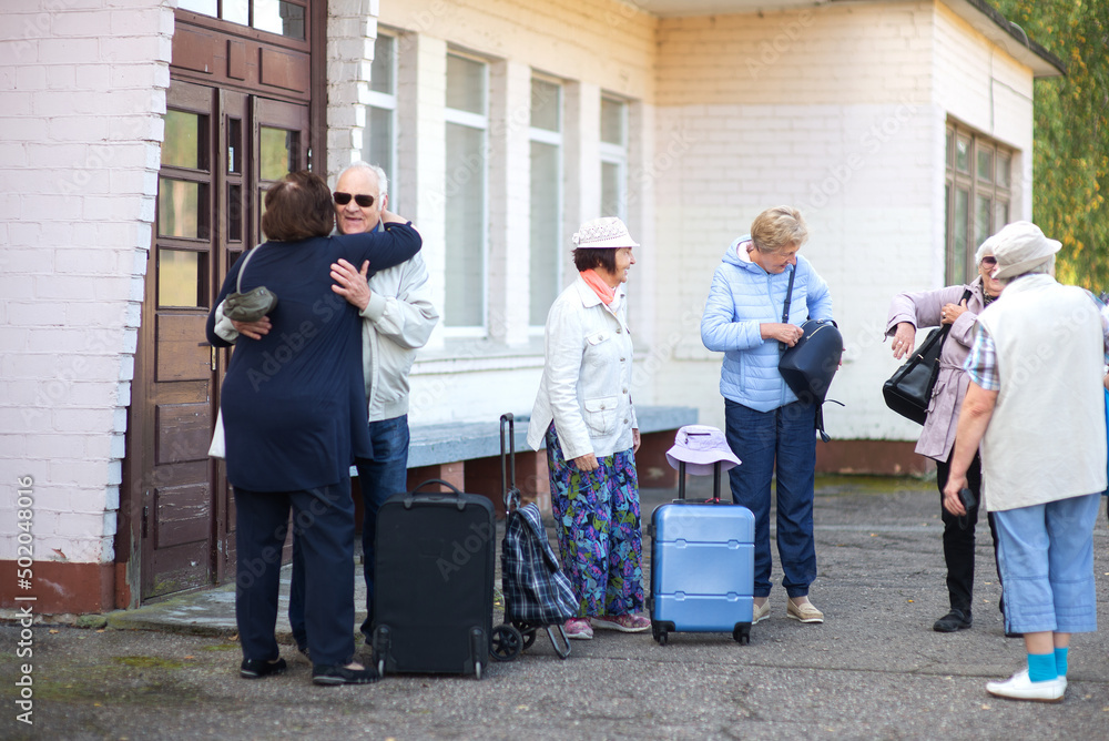 A group of elderly friends with suitcases and bags gather at the train station to go on a trip A group of elderly friends with suitcases and bags gather at the train station to go on a trip