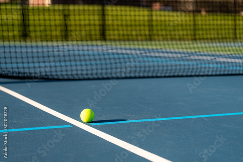 Yellow tennis ball on blue tennis court with white lines and light blue pickleball lines. © Thomas