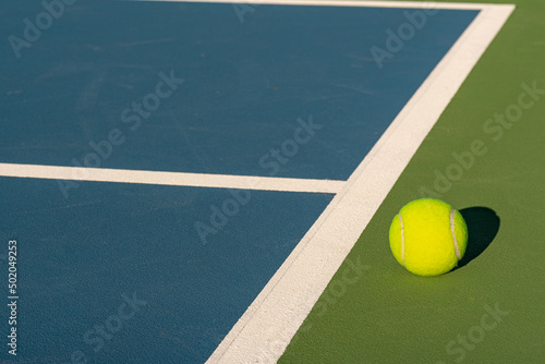 Yellow tennis ball at blue tennis court with white baseline and green out of bounds