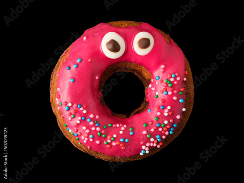 Biscuit donut with red icing and confetti with eyes on a black background
