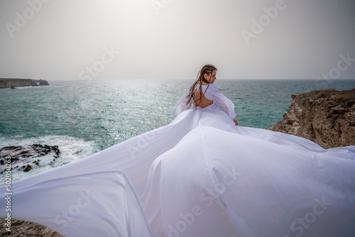 Happy freedom woman on the beach enjoying and posing in white dress. Rear view of a girl in a fluttering white dress in the wind. Holidays, holidays at sea. © svetograph