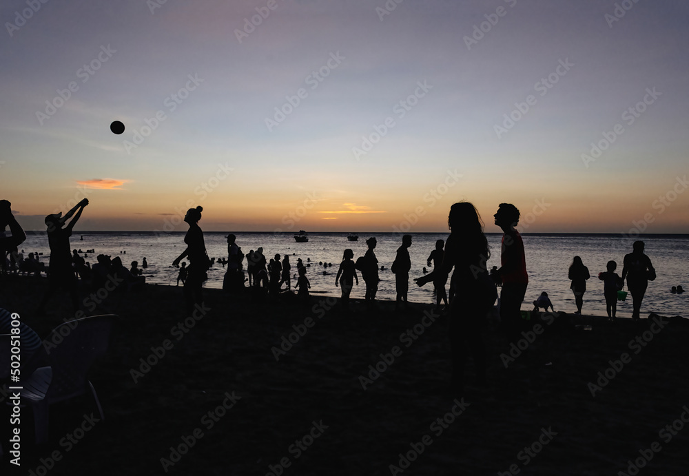 Silhouettes of people having good time on a beach, on a sunset background, with copy space.