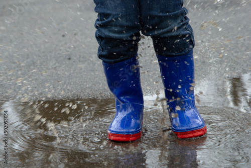 child jumping in a puddle in blue boots