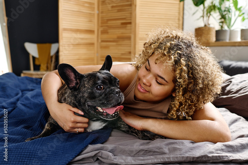 Portrait of happy smiling woman with her cute french bulldog lying on bed at morning photo