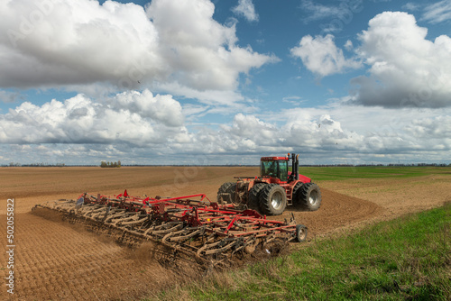 Fotografie Red tractor cultivates the farm field.