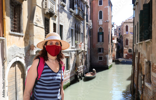 young cute woman with straw hat and surgical mask is a curious tourist in Venice