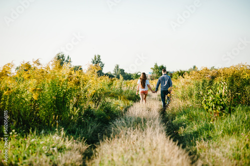 Rear view of a romantic man and woman walking on field grass, nature enjoying sunlight. Concept of lovely family holding hands. Young couple running and looking away. Back view.