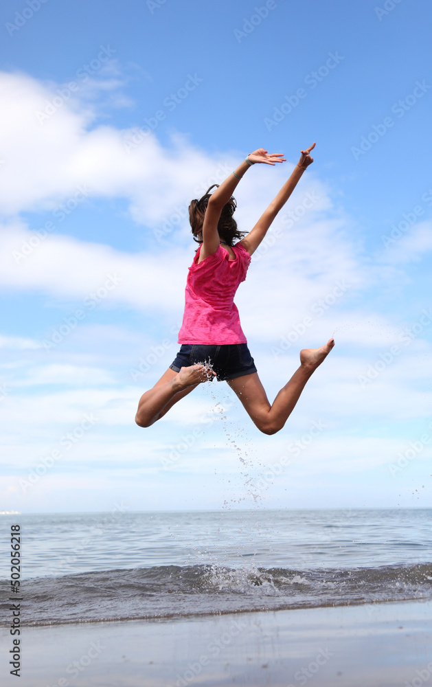girl doing a high jump of joy by the sea on the sandy beach girl doing a high jump of joy by the sea on the sandy beach