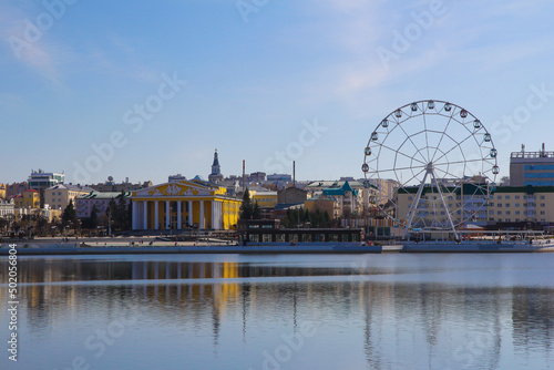 Urban landscape in the center of the city of Cheboksary, with a theater, a Ferris wheel and their reflections in the smooth surface of the bay.