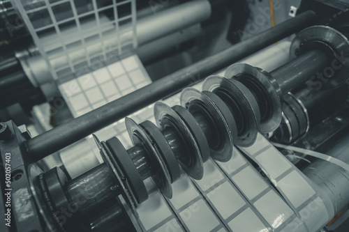 Rotating knives for cutting a self-adhesive label into several narrow ribbons. Equipment for the production of self-adhesive labels. Rotary die cutting machine with slitting blade. Selective focus