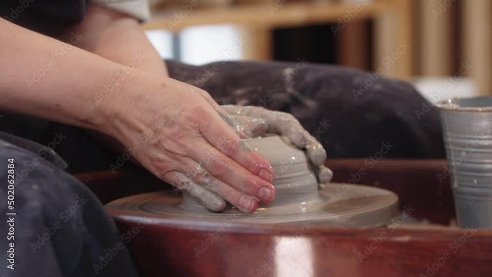 Hands of elderly woman making a hole in the piece of clay Hands of elderly woman making a hole in the piece of clay