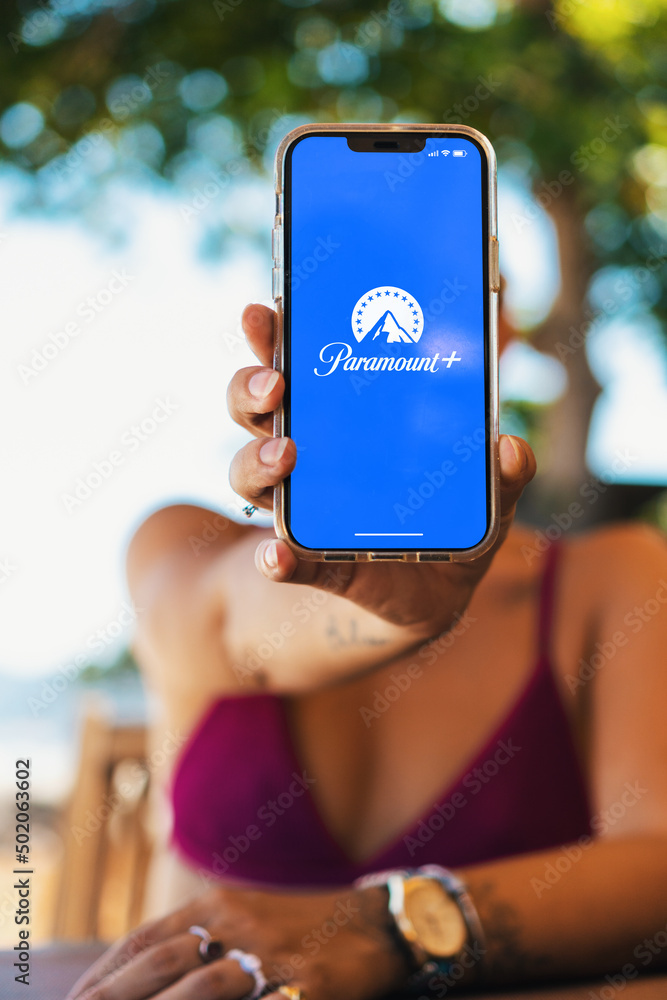 Foto Stock Girl on the beach holding a smartphone with Paramount+  (Paramount Plus) streaming app on the screen. Rio de Janeiro, RJ, Brazil.  May 2022 | Adobe Stock