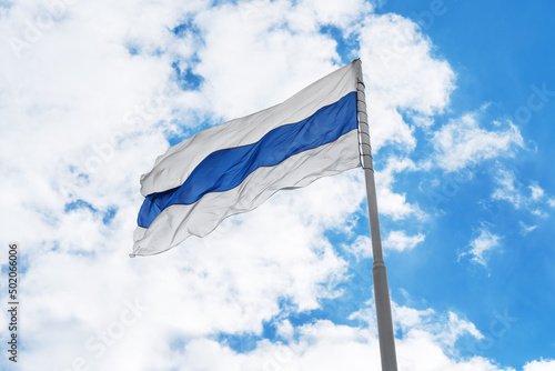Russian white-blue-white anti-war protest flag is waving in front of blue sky and clouds.