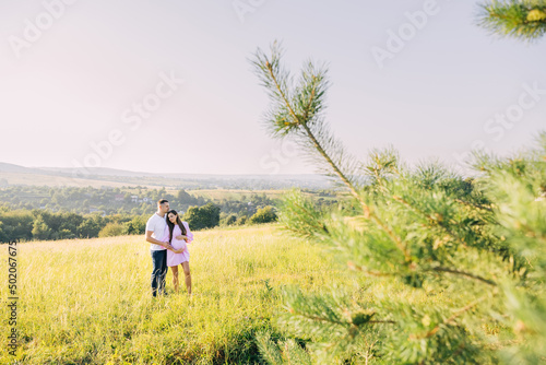 future parents, a pregnant young woman and a man touching their belly, waiting for a miracle, walking in the field, beautiful nature