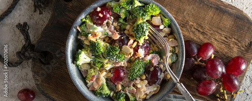 bowl with salad with broccoli, bacon, grapes and nuts on the table