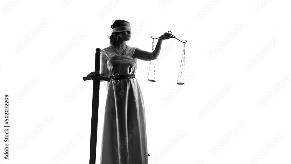 Young woman disguised as goddess of justice stands leaning on sword with one hand and holding scale with other, standing on white background in studio Young woman disguised as goddess of justice stands leaning on sword with one hand and holding scale with other, standing on white background in studio