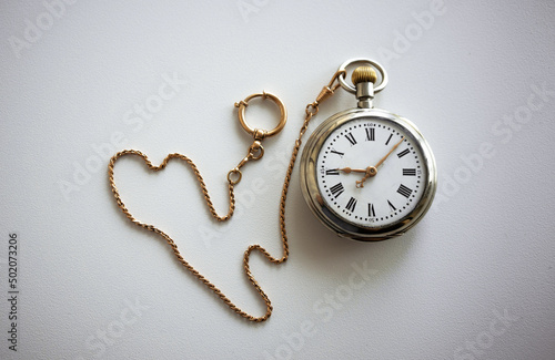 Vintage pocket watch with gold chain on white isolate. Mechanical watch with chatelaine made of gold on a white table.The passing time.