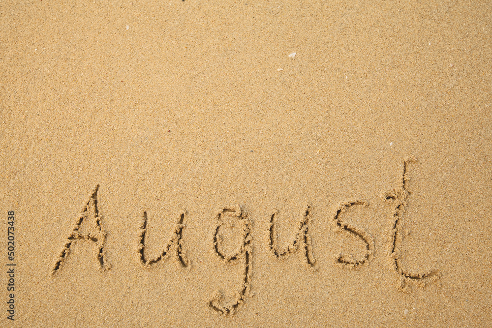 August - handwritten on the soft beach sand.