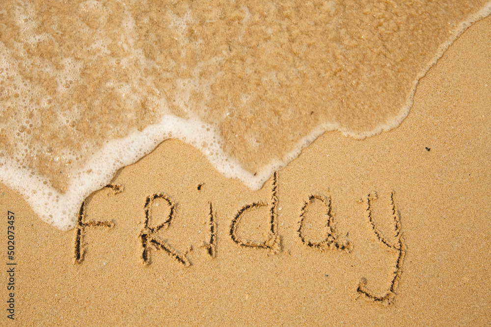 Fototapeta premium Friday - handwritten on the light beach sand with a soft wave lapping.