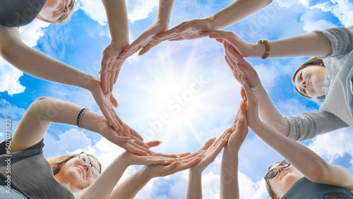 Friends make a circle with their palms against the blue sky.