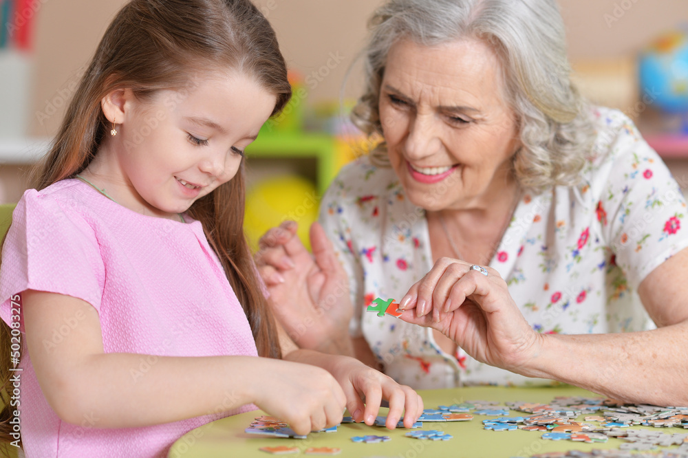 Cute little granddaughter and grandmother collecting puzzles Cute little granddaughter and grandmother collecting puzzles