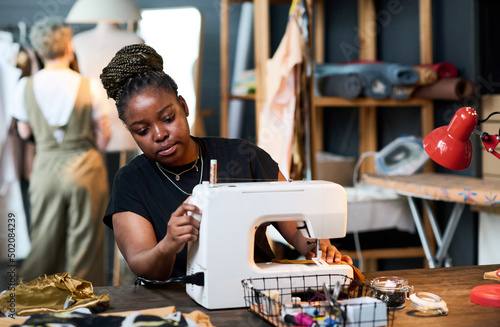 Young serious black woman in casualwear sewing new fashionable attire for clients of her boutique or creating seasonal collection of clothes