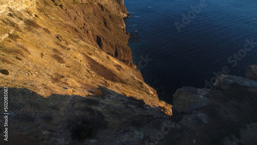 Aerial view of rocky calm ocean coast at the sunset. Shot. Beautiful view from the cliff edge on the ocean surface.