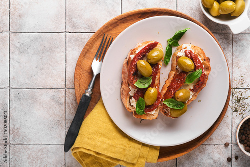 Bruschetta with sun dried tomatoes. Toast or sandwich with ricotta, sun dried tomatoes and Provence herbs with basil servered on a plate on a grey old cracked tile table. Top view banner menu recipe. photo