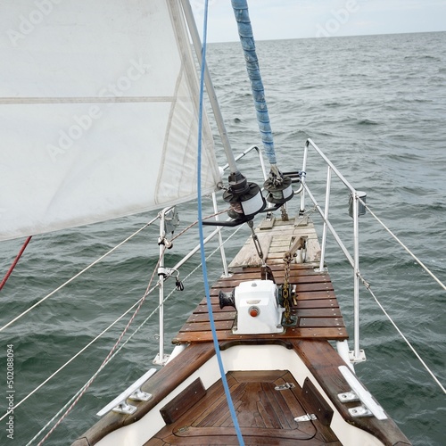 Old classic yacht sailing in an open sea during the storm. Wooden teak deck. View to the mast and sails. Ketch sailboat. Waves, water splashes. Cruise, vacations, regatta, sport, leisure activity