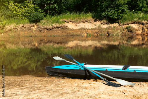 Tourist canoes with paddles stand on the river coast in summer on a water hike. Rafting on inflatable and frame double and triple kayak boats, family trip, extreme adventure in summer