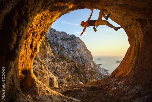 Young woman free solo climbing in cave with beautiful sea view in background photo