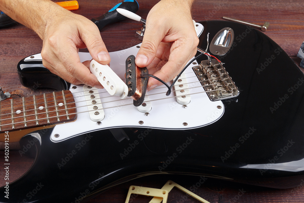 Guitar repairman selects pickup for replacement on electric guitar. - obrazy, fototapety, plakaty 