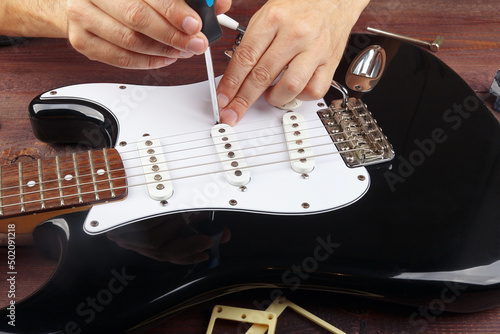Fotografie Guitar technician adjusts height pickups on black electric guitar