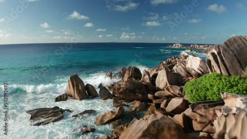 Aerial dolly over scattered granite rocks and crashing waves, La Digue