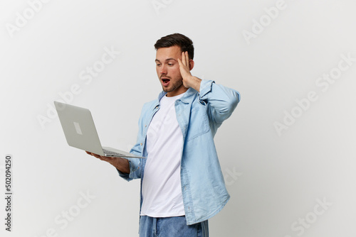 Excited shocked tanned handsome man in casual basic t-shirt have operation problems with laptop touch temple posing isolated on over white background. Copy space Mockup. Electronics repair IT concept