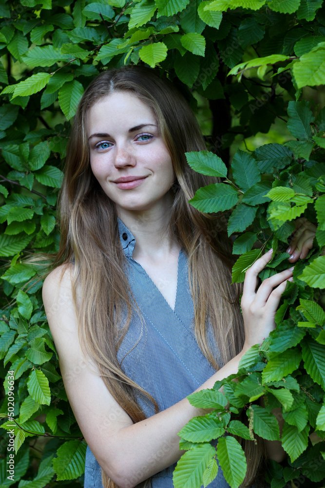 Portrait of a charming Ukrainian blonde with blue eyes, which is surrounded by green foliage. Portrait of a charming Ukrainian blonde with blue eyes, which is surrounded by green foliage.