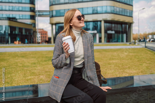 Woman holds a eco paper cup with coffee or tea and walks in spring park. Drink coffee time. Disposable paper cup. Take away. Hot beverage. Blank space. 