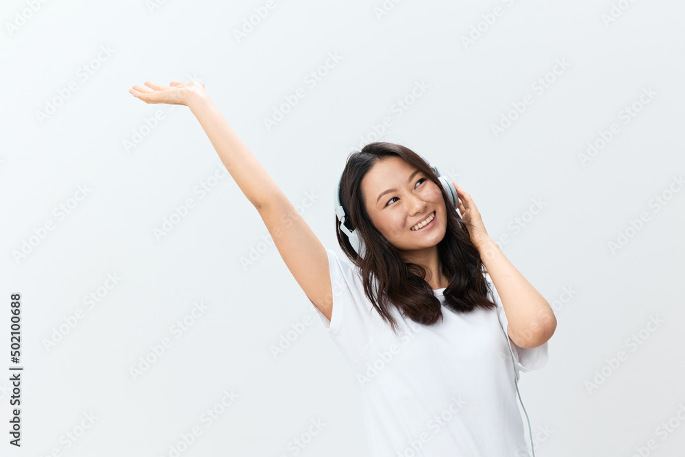 Dancing happy joyful cute Asian young female in white basic t-shirt moves to cool songs playlist posing isolated on over white studio background. The best offer for ad. Favorite Music App Ad concept Dancing happy joyful cute Asian young female in white basic t-shirt moves to cool songs playlist posing isolated on over white studio background. The best offer for ad. Favorite Music App Ad concept