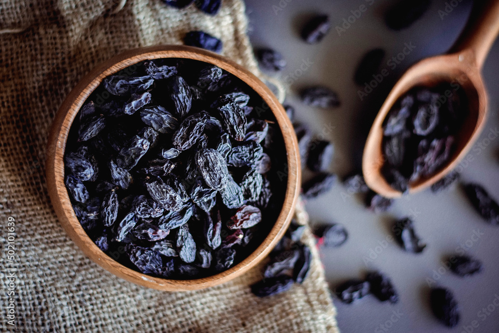 black raisins in wooden bowl with black background black raisins in wooden bowl with black background