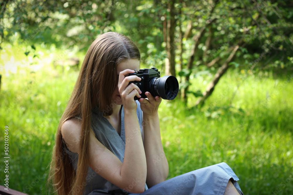 Long-haired Ukrainian woman takes pictures on a film camera of landscapes in a green park on a warm May day. Long-haired Ukrainian woman takes pictures on a film camera of landscapes in a green park on a warm May day.