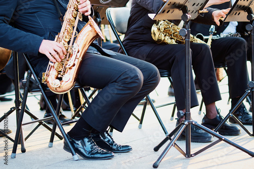 Canvas Print A group of people from a musical brass band who are sitting on chairs and playing music, jazz on golden brass pipes, sitting outside in the open air